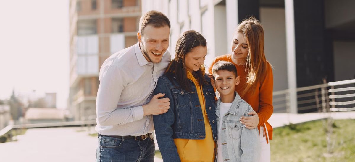 Delighted family in trendy casual wear holding each other and standing near modern building on city street while walking together during weekend