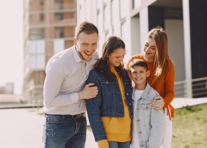 Delighted family in trendy casual wear holding each other and standing near modern building on city street while walking together during weekend