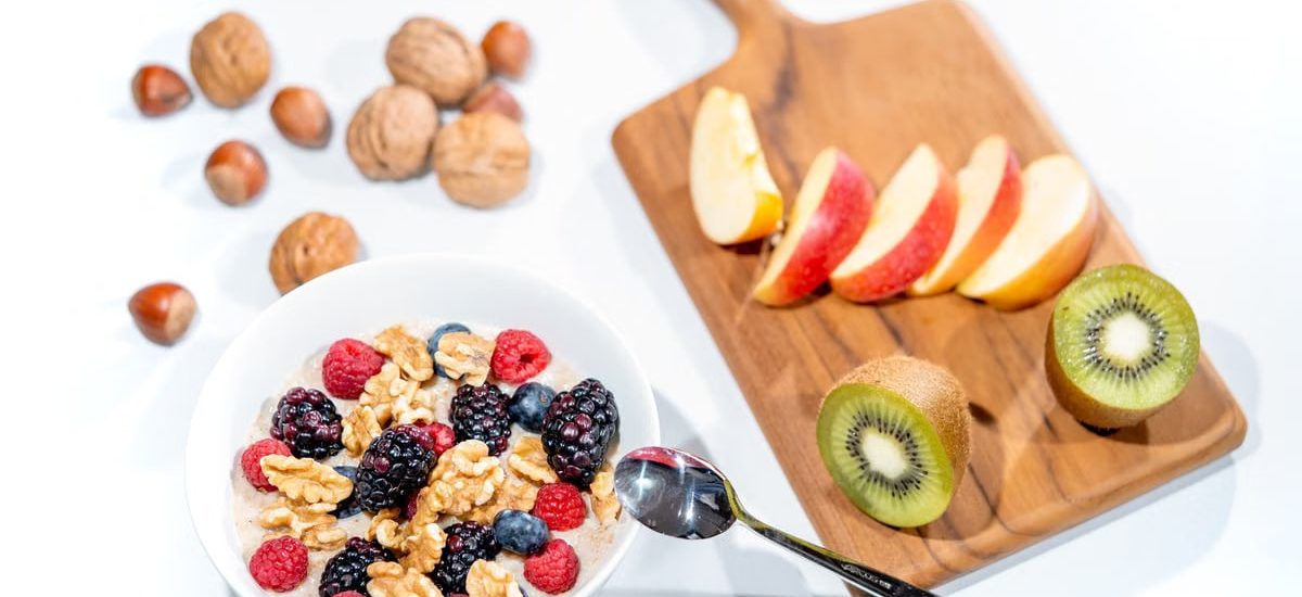 A nutritious breakfast bowl featuring fresh berries and walnuts, served with sliced fruit and kiwi.